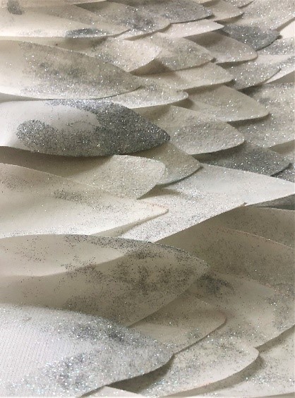     Fotografia 9 ukazuje rzędy białych piór wykonanych z materiału i pokrytych srebrnym brokatem