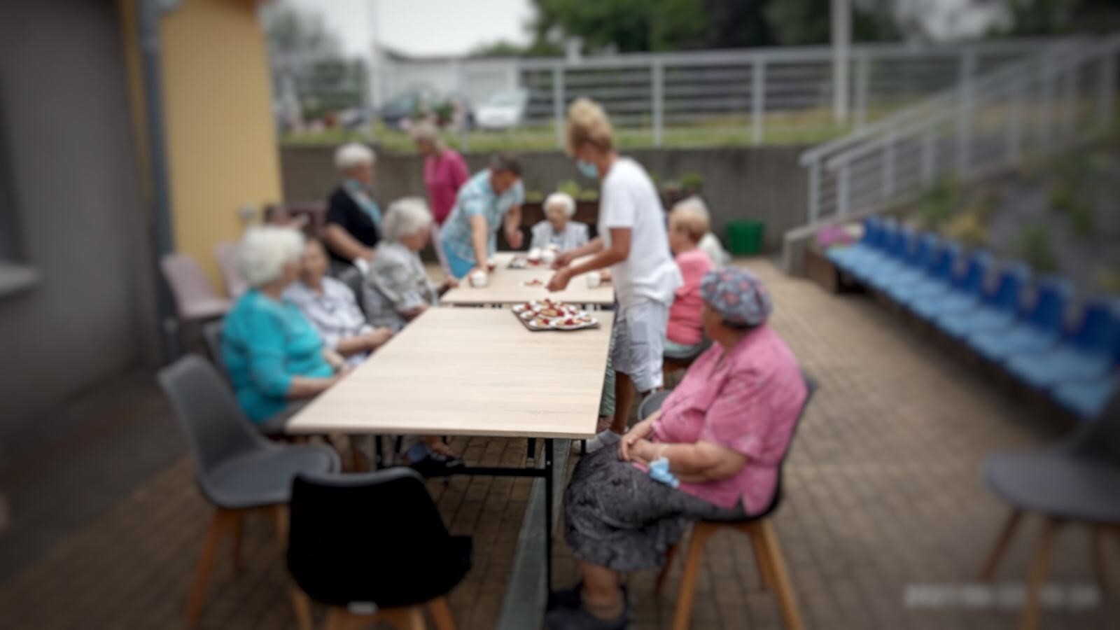 Teren zewnętrzny DDP. Rozłożone stoły ogrodowe, przy których siedzą klienci Ośrodka w oczekiwaniu na truskawkowy deser.