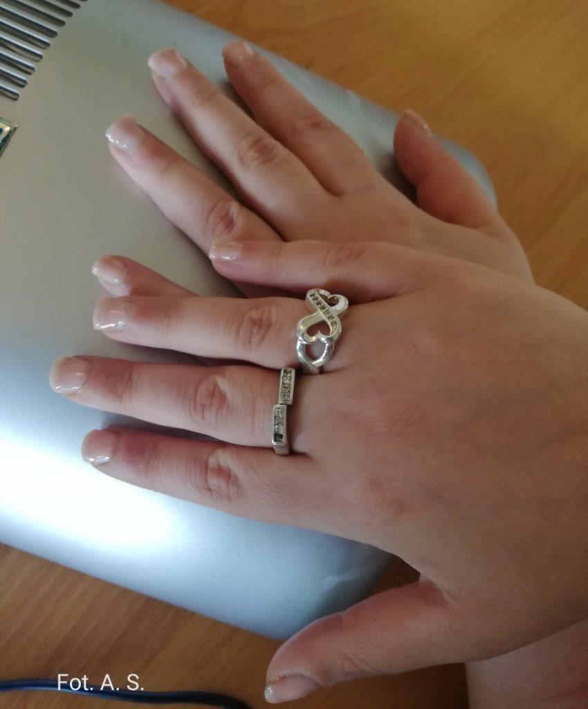 Zdjęcie dłoni kobiecych ułożonych na lampie uv do manicure, na prawej dłoni dwa srebrne pierścionki. Płytka paznokcia w kolorze naturalnym
