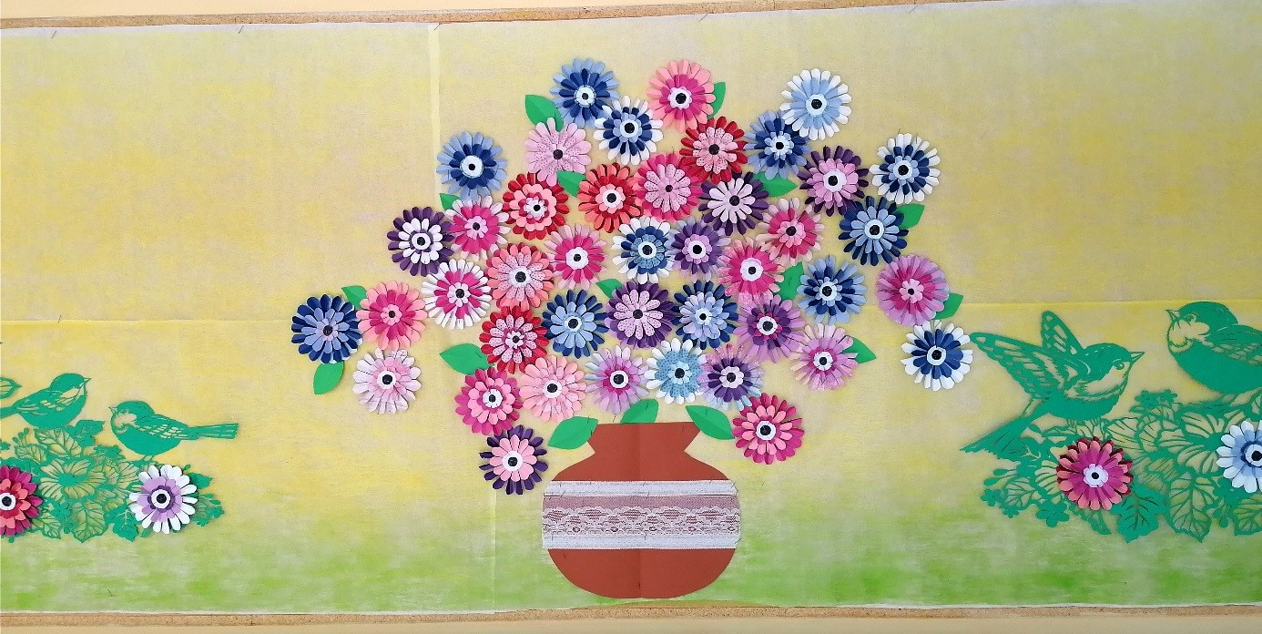 Na zdjęciu kwiaty ręcznie robione w różnych kolorach, ułożone w wazonie. Wszystko robione z papieru hobbystycznego