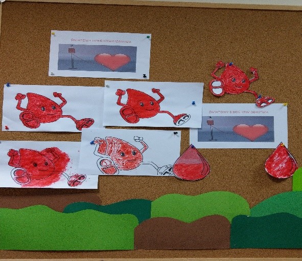 Fotografia przedstawia kilka prac klientów dziennych domów pomocy, na białych kartkach widnieje pokolorowany symbol czerwonej kropli krwi z rączkami i nóżkami