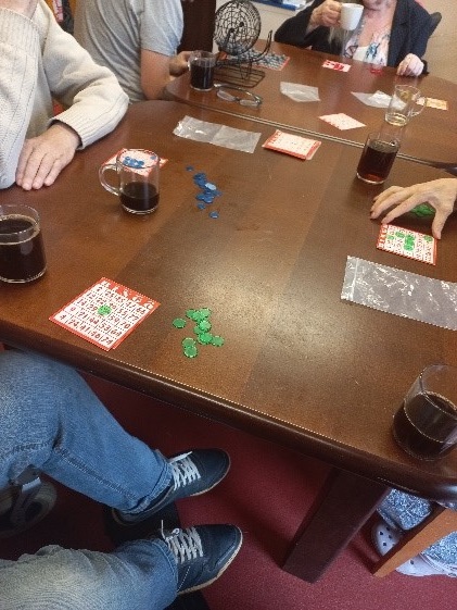  Zdjęcie. Przedstawia mieszkańców grających w grę Bingo oraz kubki z kawą.
