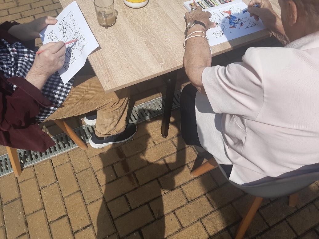 Obchody Dnia Czerwonego Kapturka. Klienci siedzą przy drewnianym stole na świeżym powietrzu, wypełniają kredkami kolorowanki o Czerwonym Kapturku
