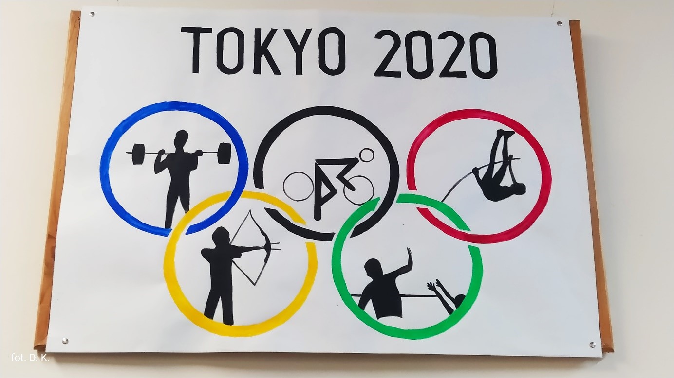 Plakat Igrzysk Olimpijskich z napisem Tokio 2020, w kolorowych kołach olimpijskich namalowane piktogramy dyscypliny sportowych, od góry od lewej strony kolejno: niebieskie koło- podnoszenie ciężarów, czarne koło – kolarstwo, czerwone koło – skok o tyczce, poniżej od lewej, żółte koło – łucznictwo, zielone koło – piłka siatkowa