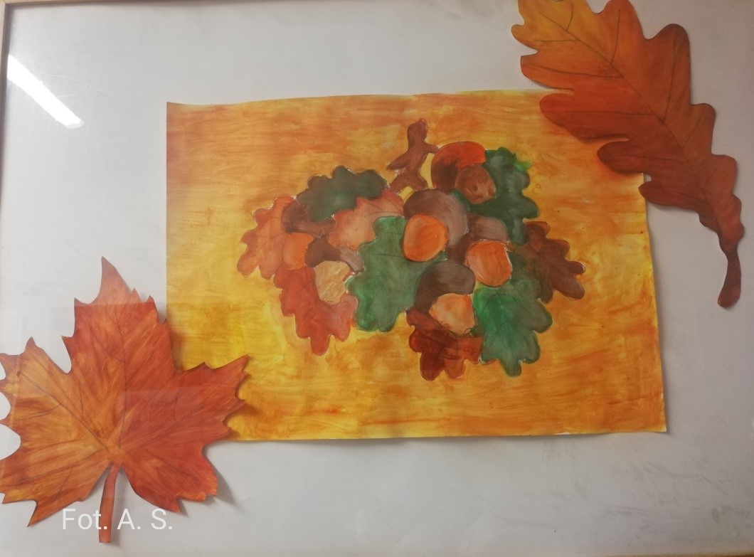 Na zdjęciu jesienna kompozycja prac plastycznych mieszkańców: liść klonowy, liść dębowy, gałązka dębu z żołędziami wszystko w kolorach pomarańczowym, zielonym, brązowym, żółtym, czerwonym