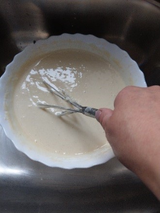 na fotografii widać białą miskę z ciastem naleśnikowym, trzepaczkę do mieszania oraz dłoń
