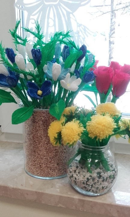fotografia Przedstawia 2 wazony z kwiatami  - po lewej stronie z białymi i granatowymi krokusami, po prawej z żółtymi mleczami i różowymi pąkami róż. Kwiaty wykonane z bibuły