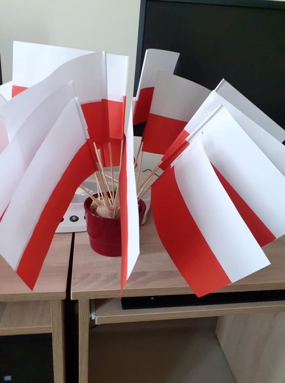 Zdjęcie 4 Nasze flagi. Na zdjęciu widzimy wykonane na zajęciach przez klientów biało czerwone flagi. Flagi wetknięte w naczynie stojące na jasnym blacie biurka.