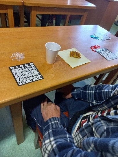 Zdjęcie nr 4. Na głównym planie mamy stół a na nim plansze bingo, kubek oraz ciastko.