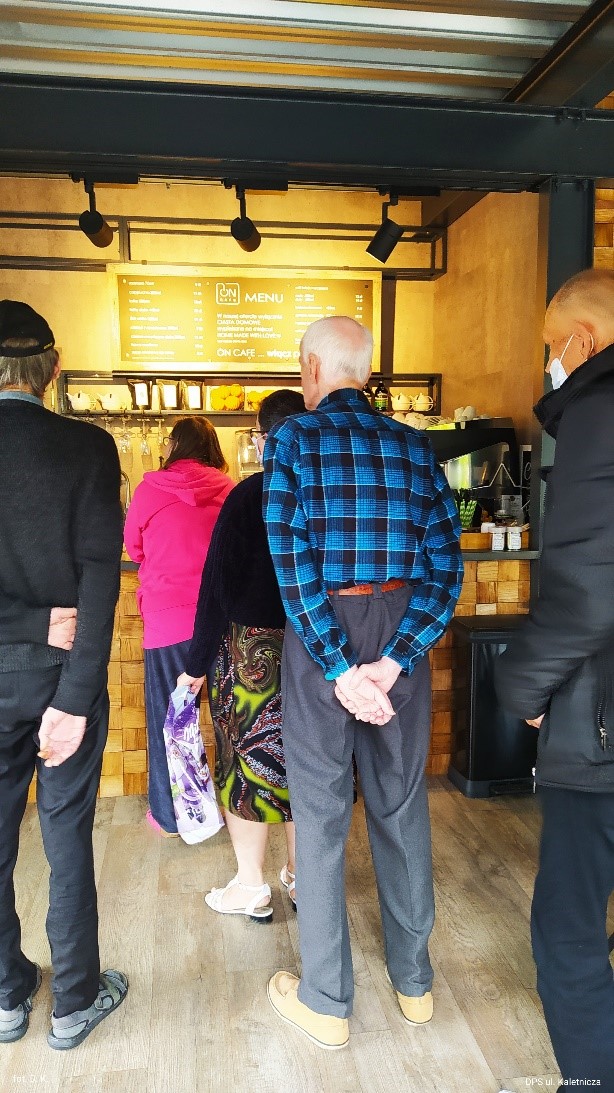 Na zdjęciu wnętrze kawiarni a w niej grupa mieszkańców stojąca w kolejce do kasy