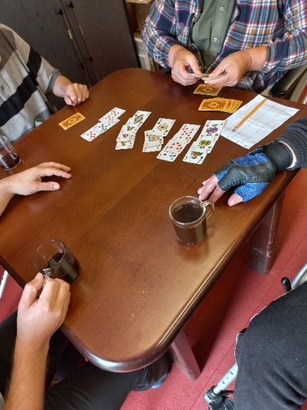 Zdjęcie nr.16 Zdjęcie przedstawia mieszkańców grających w karty na brązowym stole. 