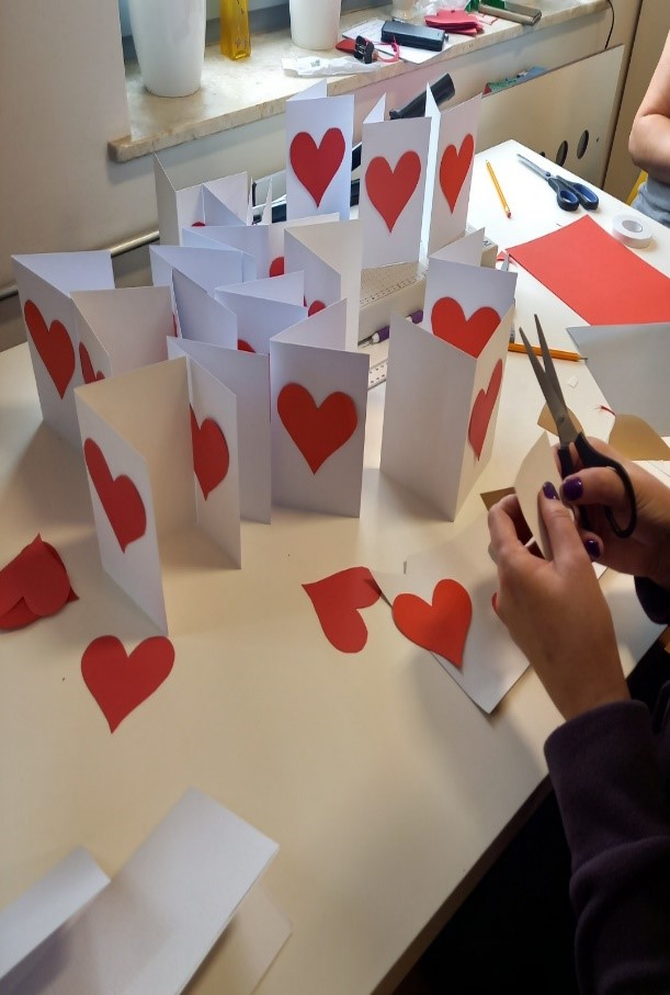 Ręczne zdobienie i dekorowanie kartek z okazji obchodów Międzynarodowego Dnia Chorego.  Na białym gładkim papierze,  czerwone i złote serca