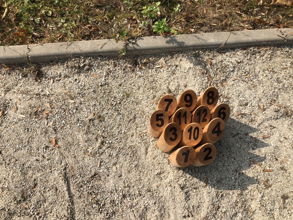 Na zdjęciu fińskie drewniane kręgle z wypalonymi liczbami od 1 do 12, które stoją na boisku z piasku