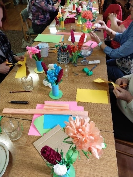 Zdjęcie przedstawia stolik z różnymi przedmiotami-kartki, kwiaty, nożyczki